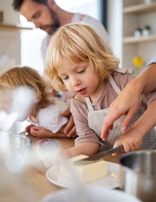 Young family with two small children indoors in kitchen, preparing food.